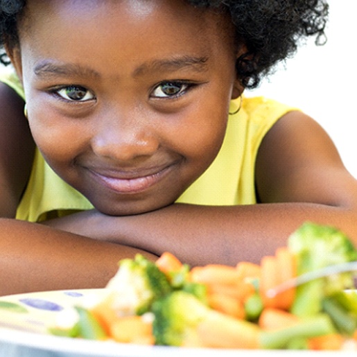 A little girl smiling with a plate full of vegetables in front of her