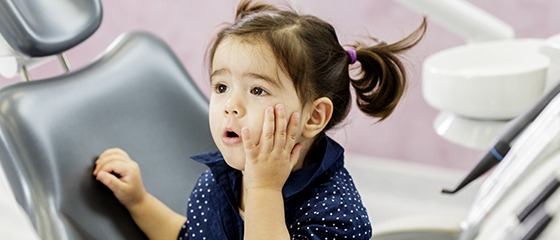 Little girl in dental chair holding cheek