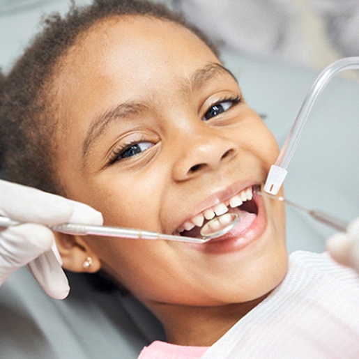 A little girl lying back in a dentist’s chair and having her teeth checked and cleaned