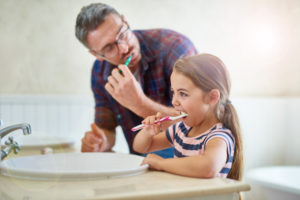 Father teaches daughter toothbrushing skills as recommended by Willow Park children's dentist