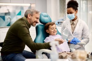 smiling autistic child enjoying special needs dentistry with his dad 