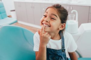 young girl pointing to her smile while visiting her pediatric dentist in Willow Park
